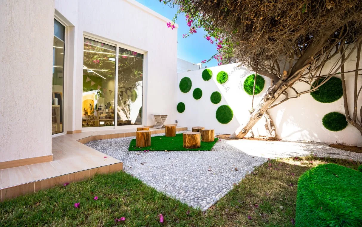 A calm Montessori outdoor space with tree stumps, pebbles, real grass and a planted bougainvillea wall.