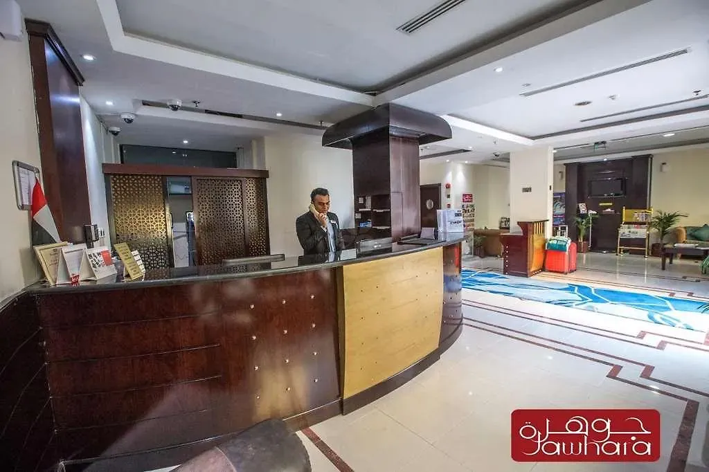 Reception desk at Al Jawhara Metro Hotel with the Jawhara wordmark and fresh flowers