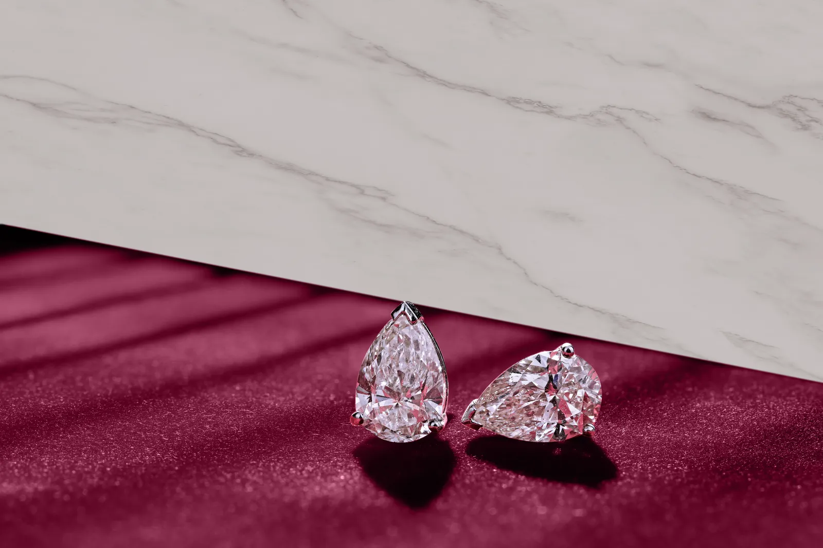 Pear-cut diamond studs by Dhakan on marble and maroon