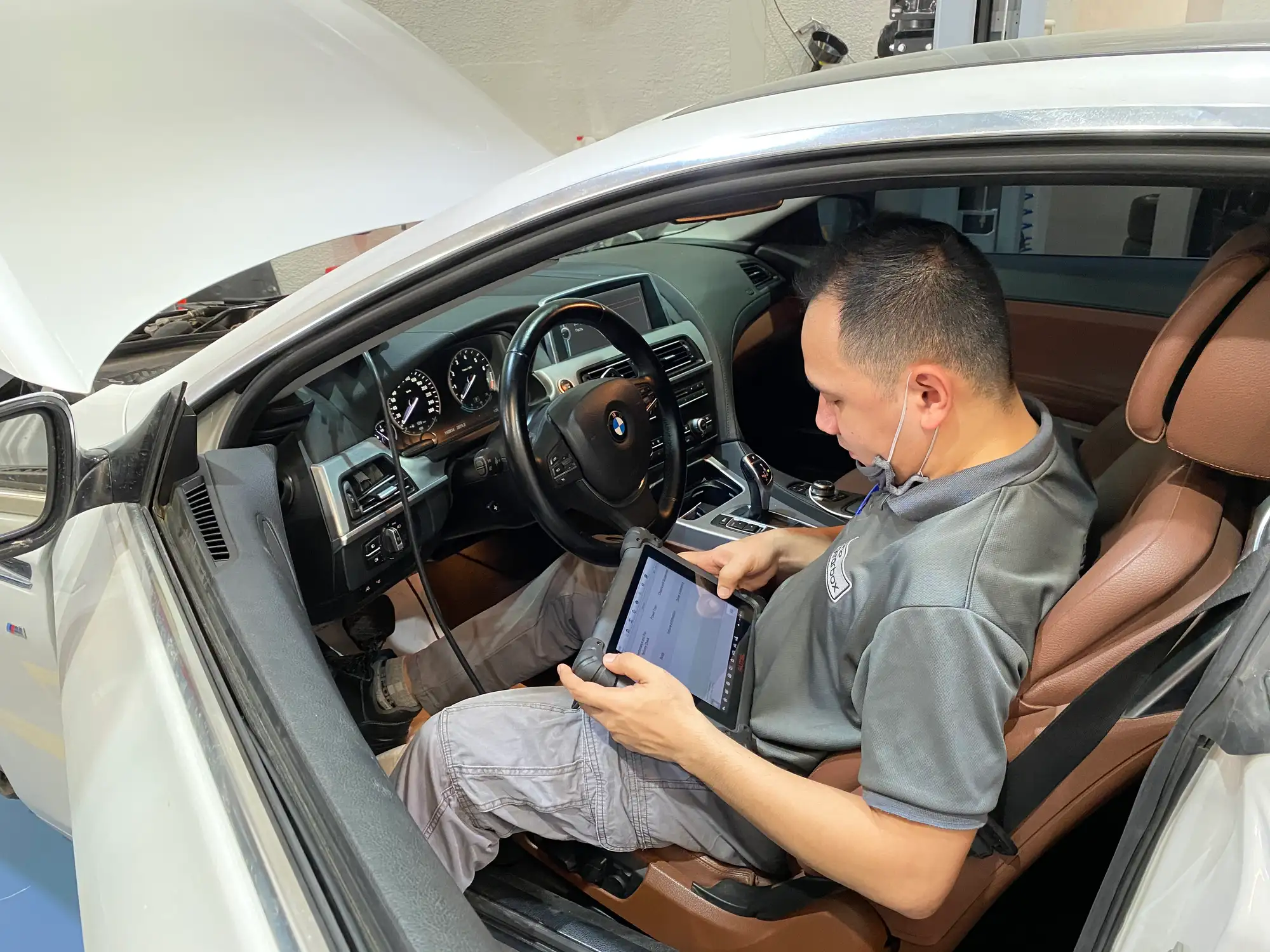 A gearbox technician running tablet diagnostics inside a BMW