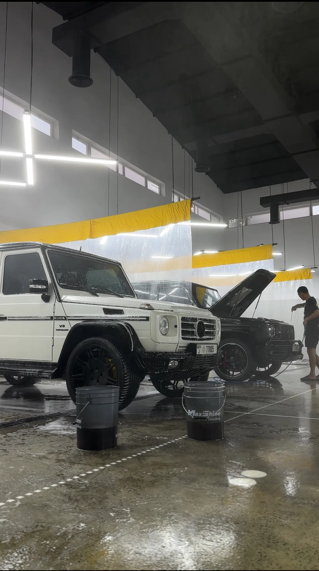 Two SUVs being detailed in BAZA's wash bay under yellow drapes