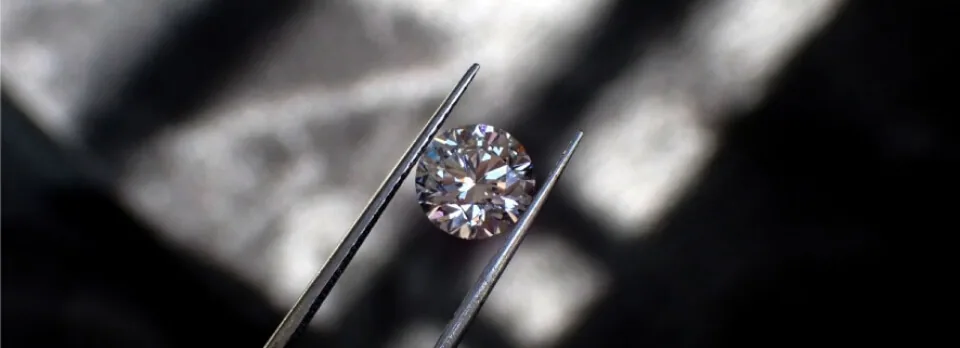 A natural diamond held in tweezers under showroom light