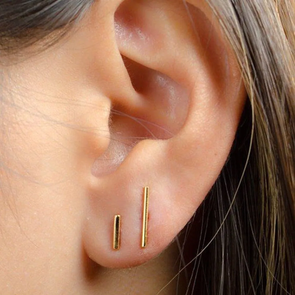 A pair of minimal gold bar studs worn in the ear