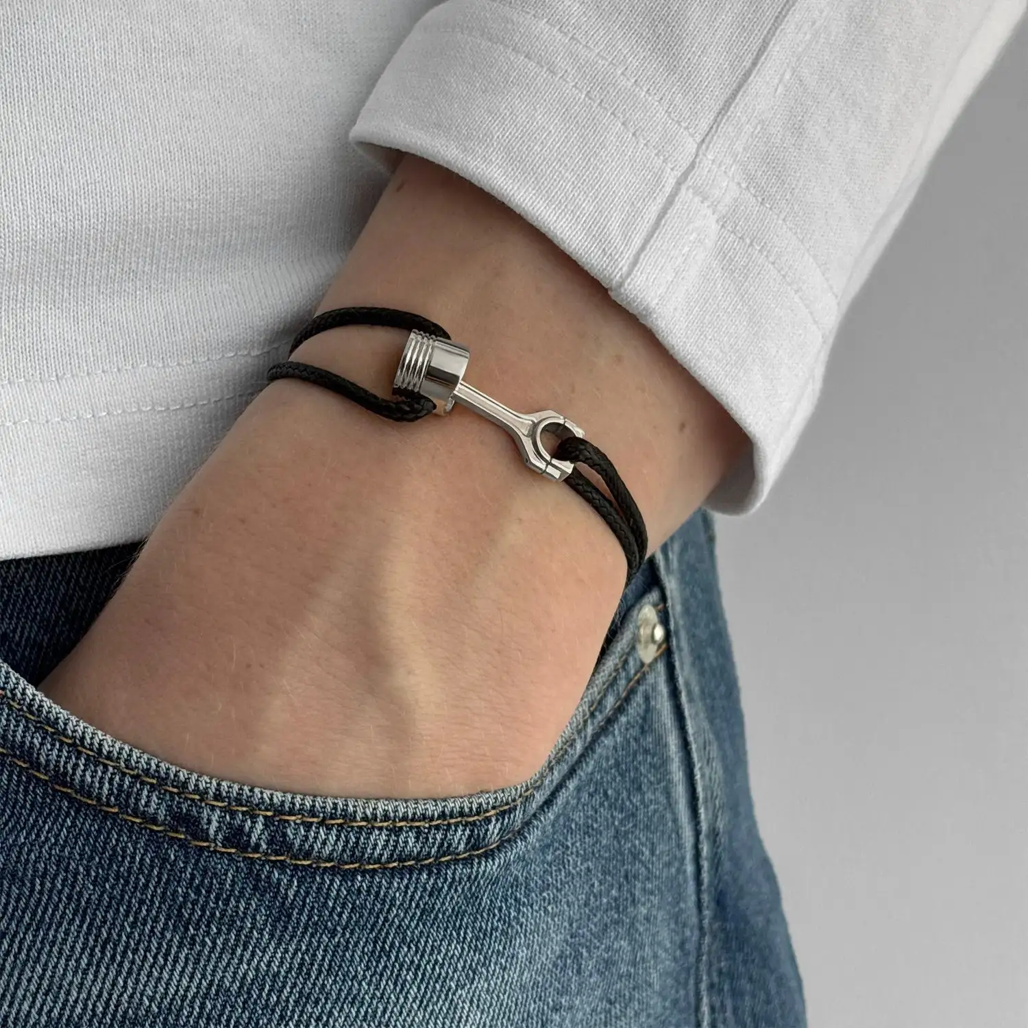 A silver piston-clasp cord bracelet worn on the wrist.