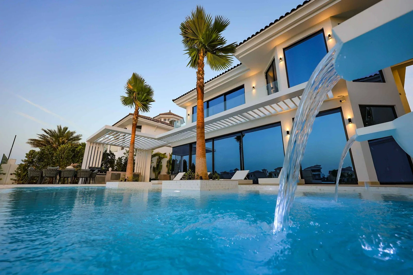Twilight villa with a turquoise infinity pool, water feature and palms in Dubai