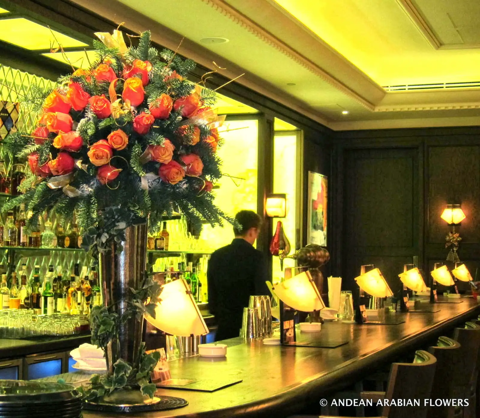Tall arrangement of orange roses and seasonal greens in a luxury hotel bar
