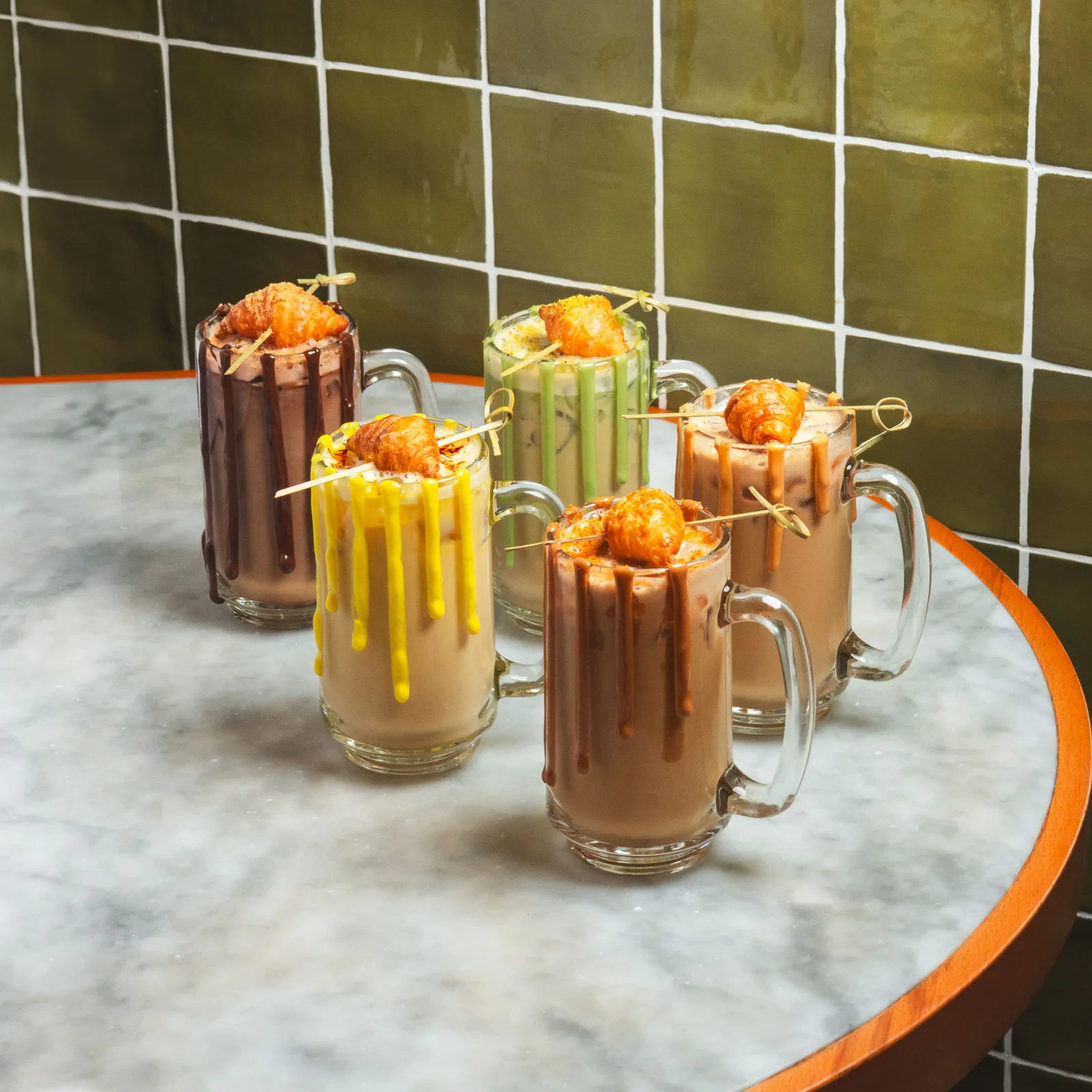 A line-up of croissant-topped iced lattes in chocolate, pistachio, caramel and saffron