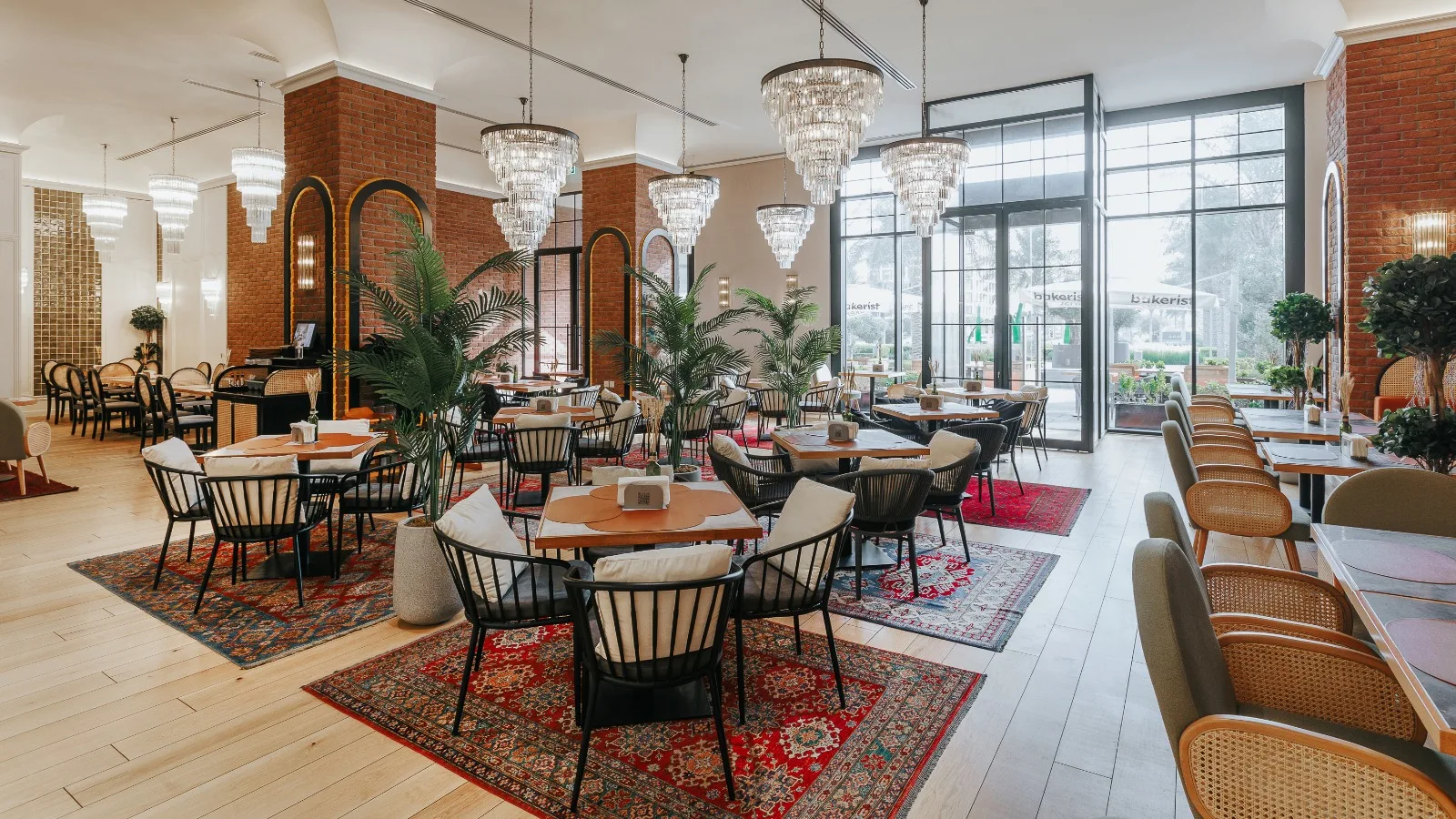 Bakerist's dining room with chandeliers, exposed brick, palms and Persian rugs