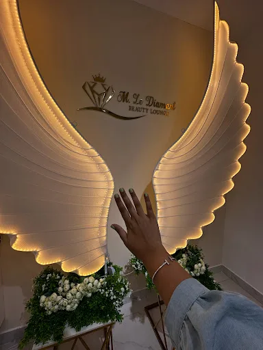The gold illuminated angel-wing feature wall beneath the M Le Diamant Beauty Lounge mark, dressed with white florals