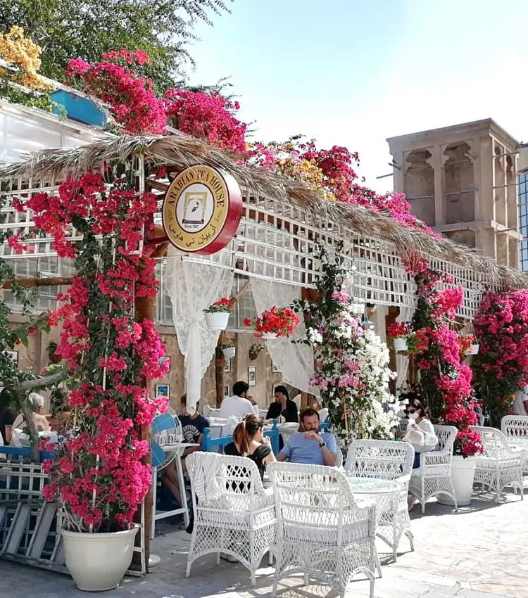 The Arabian Tea House courtyard draped in pink bougainvillea, with the venue's round sign and a traditional wind tower behind