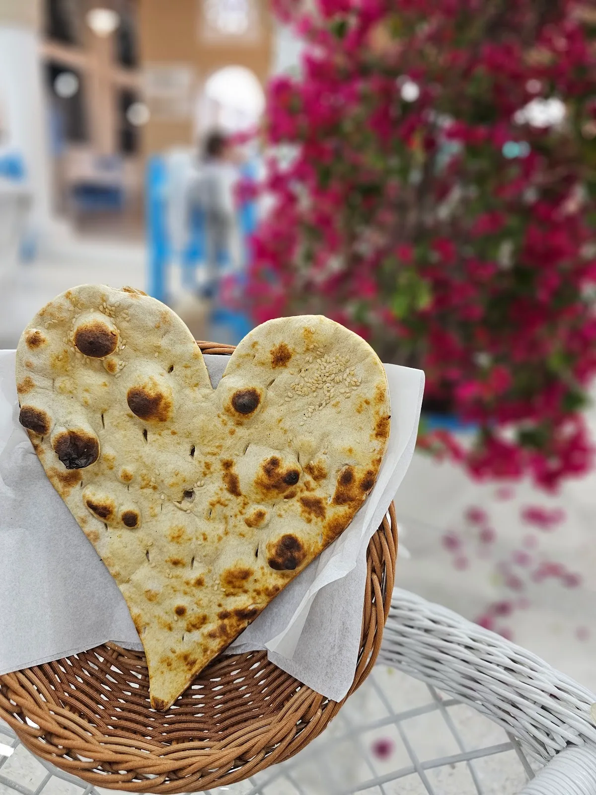 A heart-shaped flatbread resting in a wicker basket beside pink bougainvillea