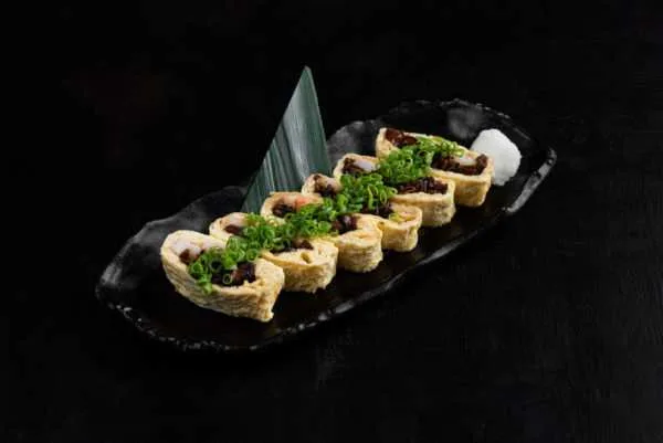 Fried tofu rolls topped with scallion on a black plate