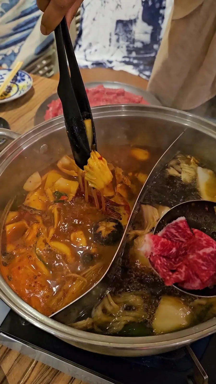 Split-broth shabu-shabu hotpot being served at the table