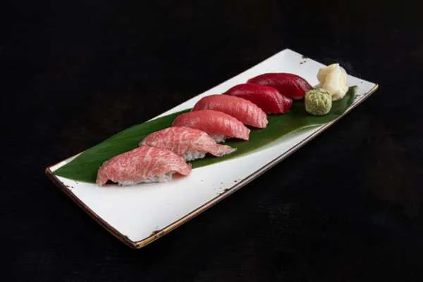 Premium fatty tuna nigiri on a white plate with a bamboo leaf