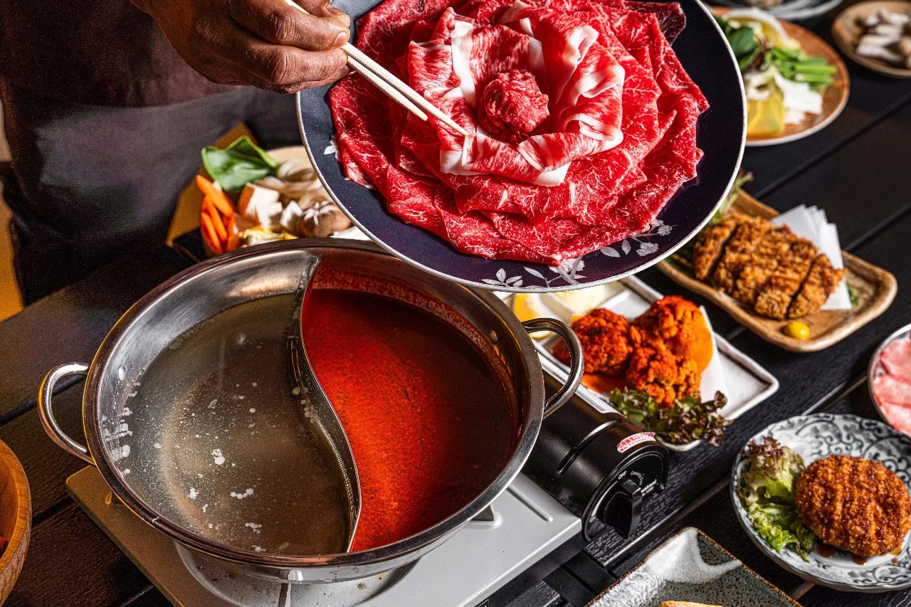 A4 wagyu being lowered into a split-broth shabu-shabu hotpot, surrounded by side dishes at Kimuraya