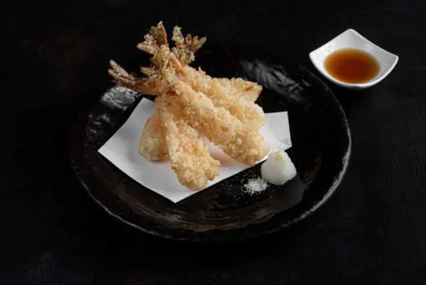 Golden prawn tempura on a black plate with dipping sauce