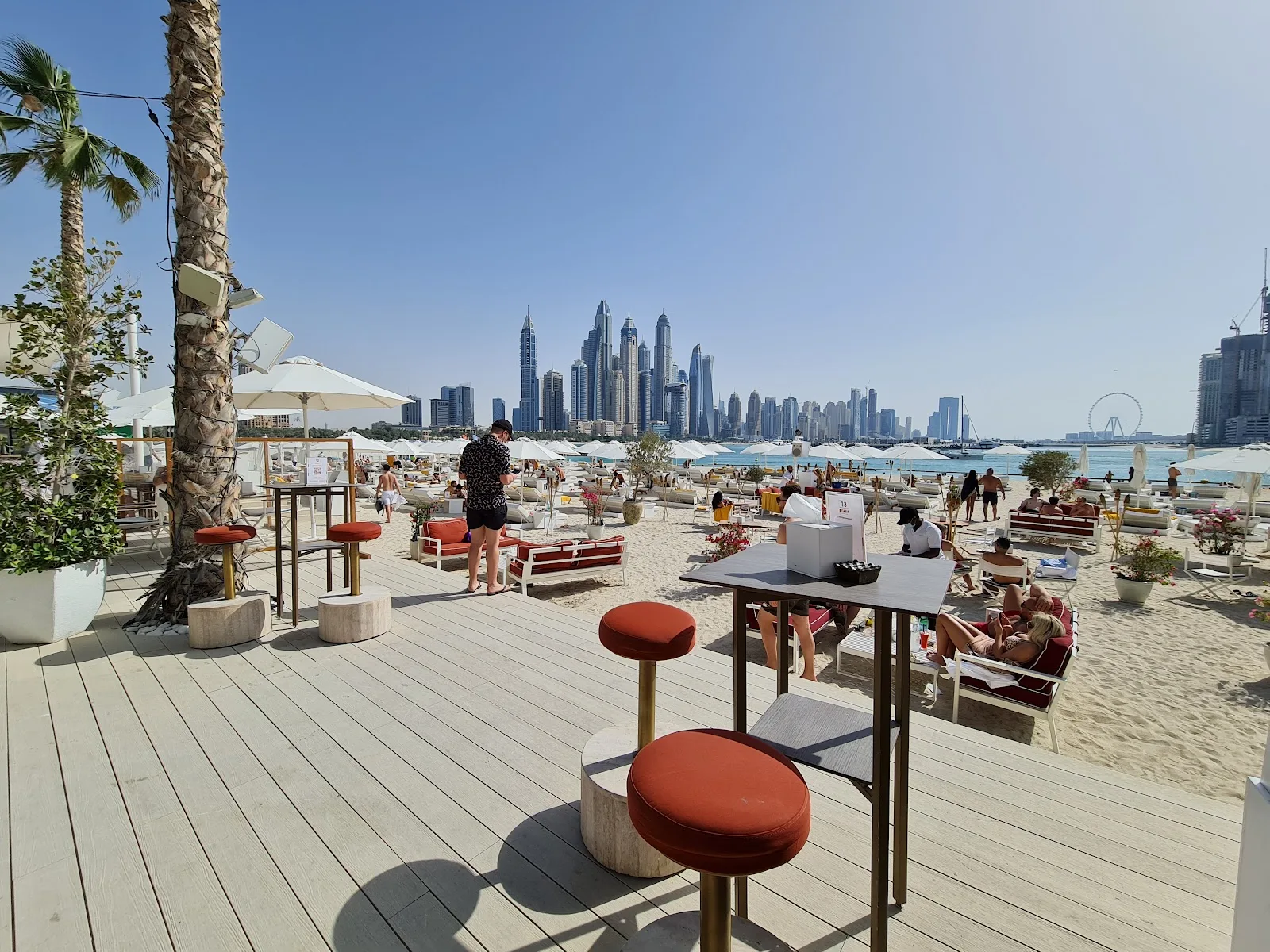 Beach deck at Praia with terracotta bar stools, palms and the Dubai Marina skyline across turquoise water