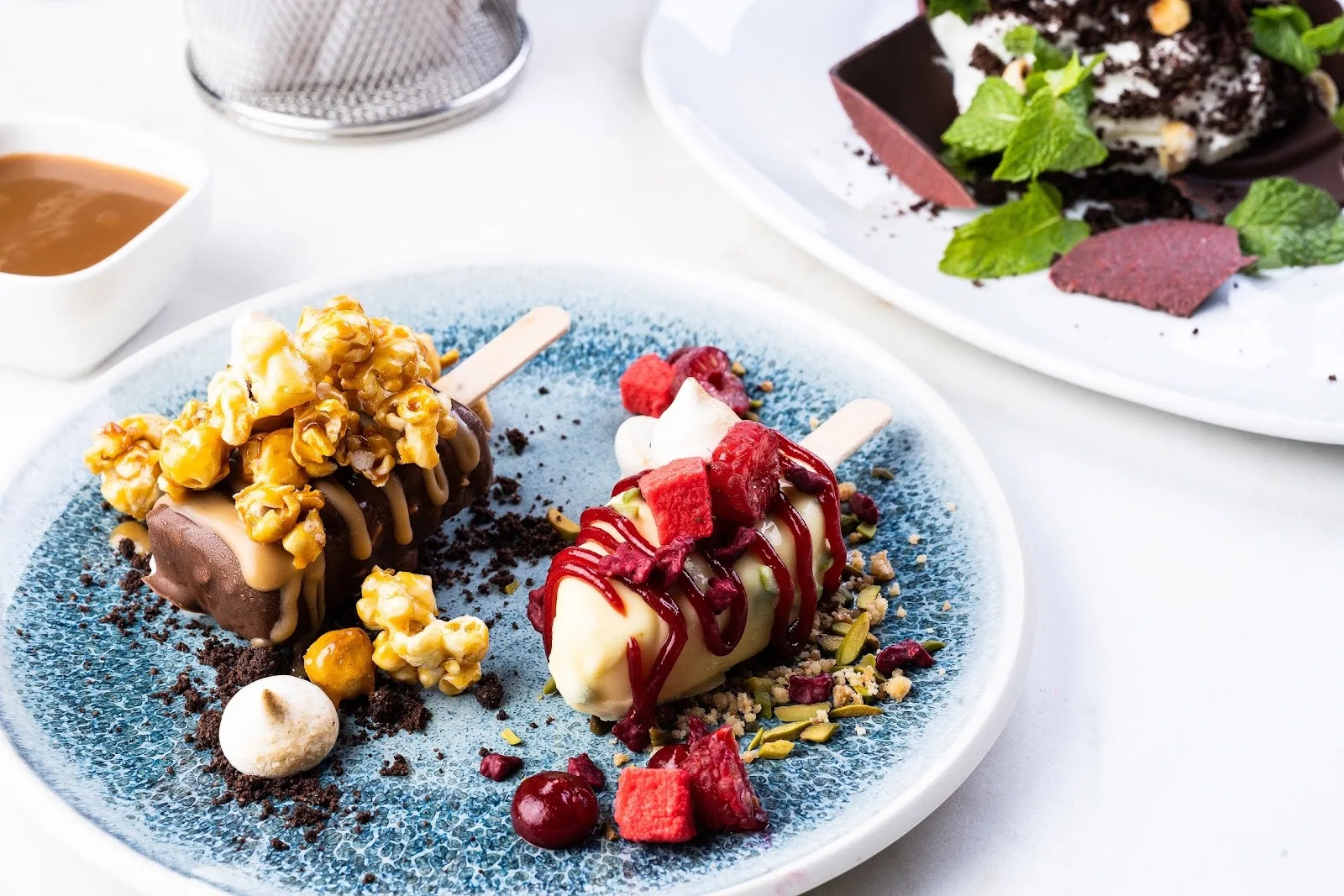 Two artful ice-cream desserts with caramel popcorn and berries on a ceramic plate