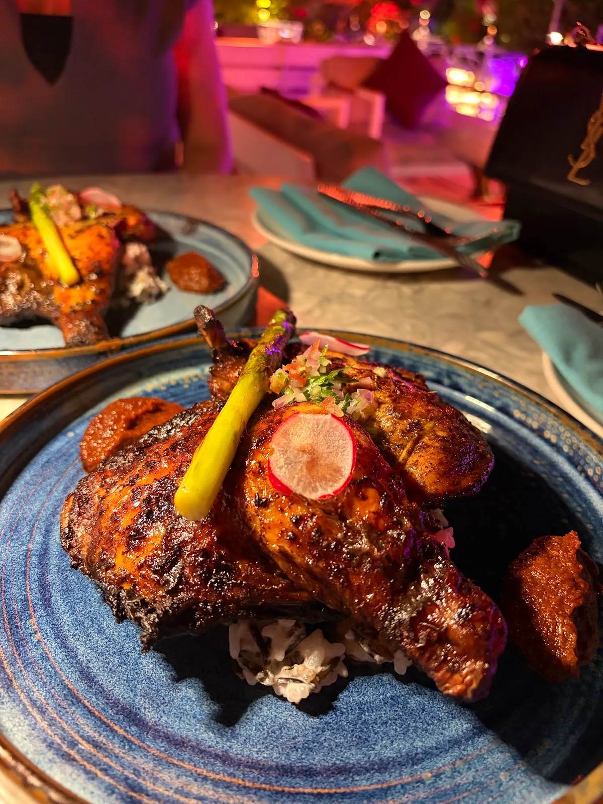 Char-grilled spiced chicken plated on a blue ceramic plate in a moodlit lounge