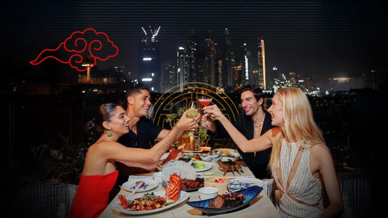 Guests raising cocktails over a seafood spread at Praia with the Dubai skyline glowing at night