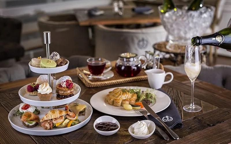 Tiered afternoon tea spread with pastries, sandwiches, tea and sparkling wine