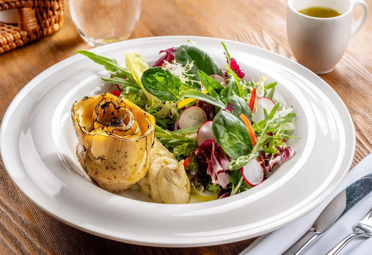 Grilled artichoke with garden salad on a white plate