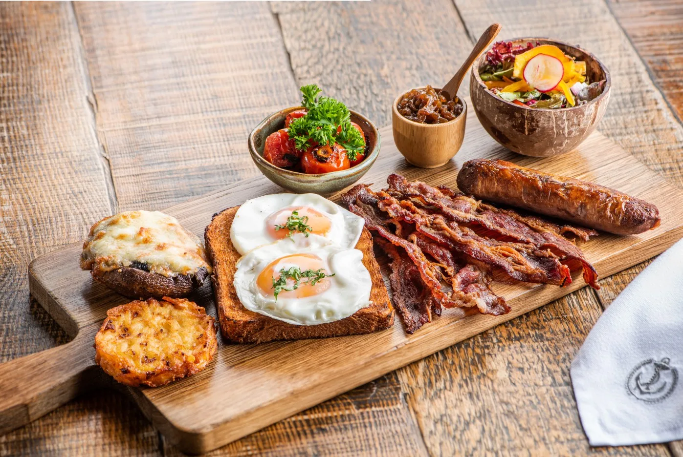 Full breakfast served on a wooden board with eggs, bacon, sausage and sides