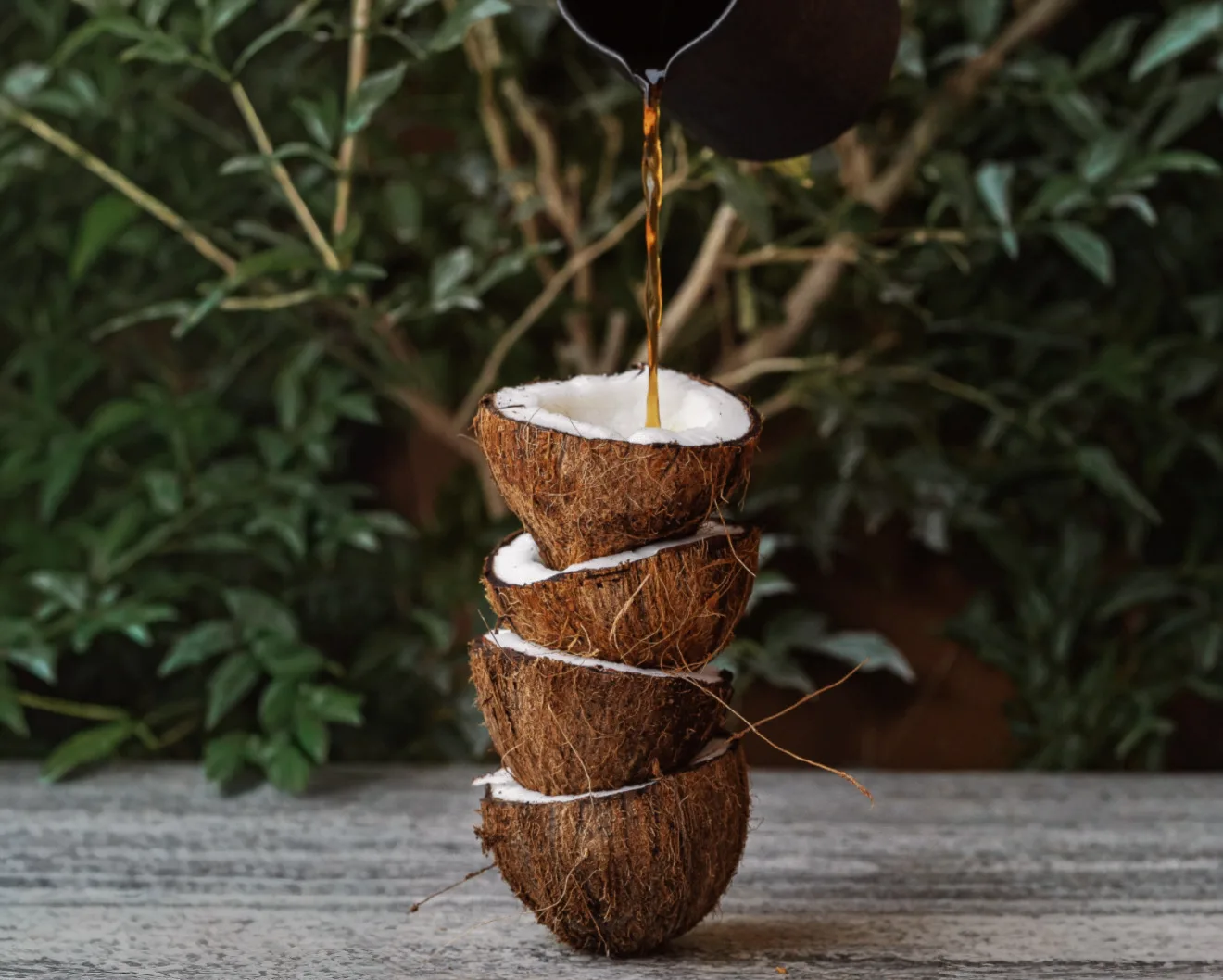Coffee being poured into stacked coconut shells against a leafy backdrop