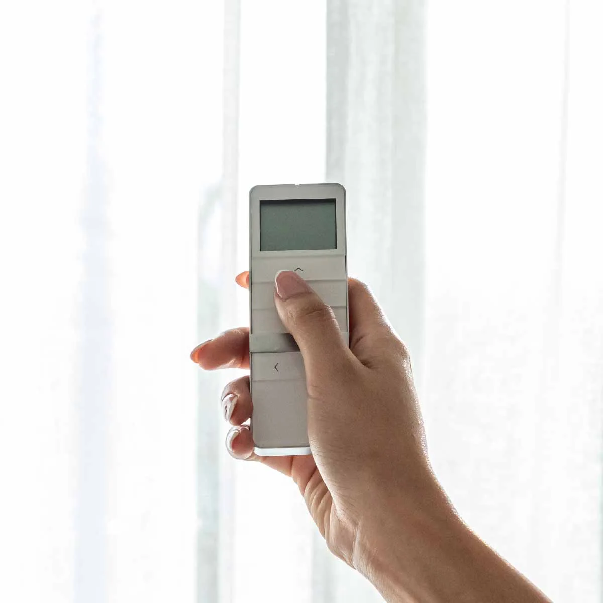 A hand using a remote to operate motorised curtains