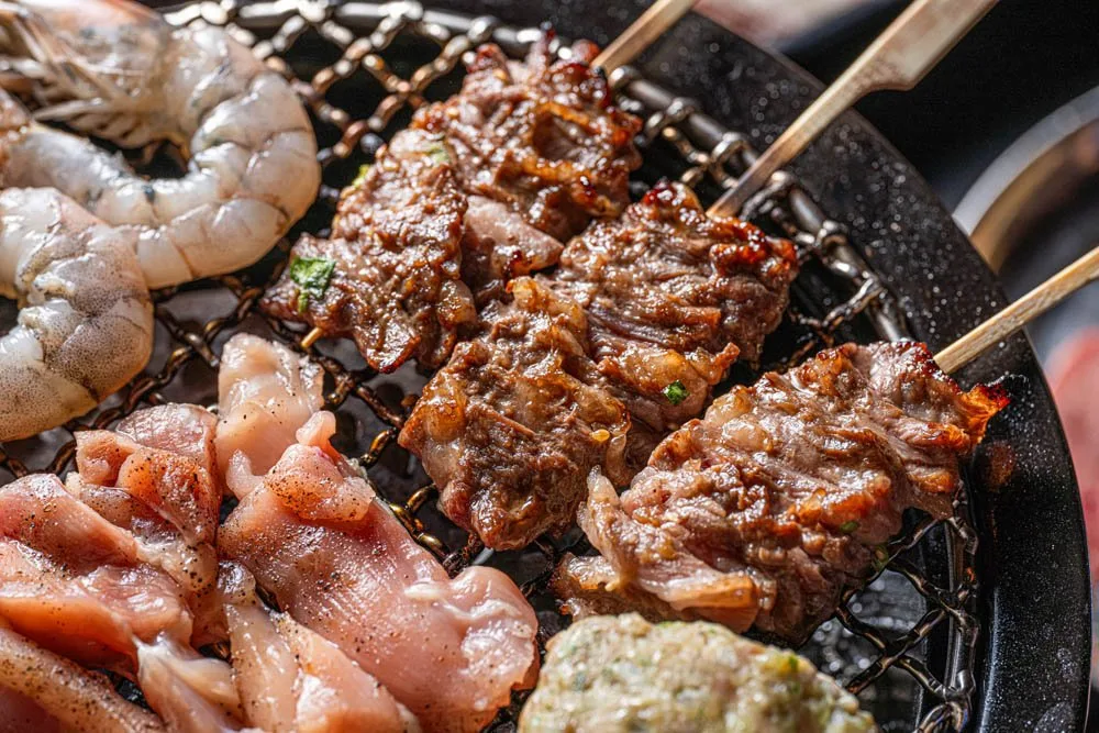 Close-up of marinated beef, prawns and chicken on a tabletop charcoal grill