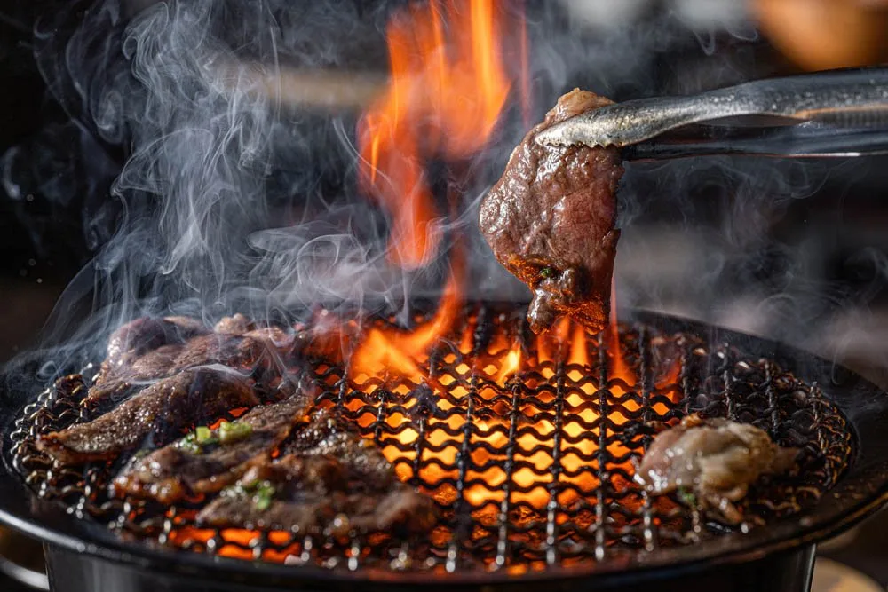 Charcoal robata grill flaming over a spread of marinated meats and seafood at Mogi-ya