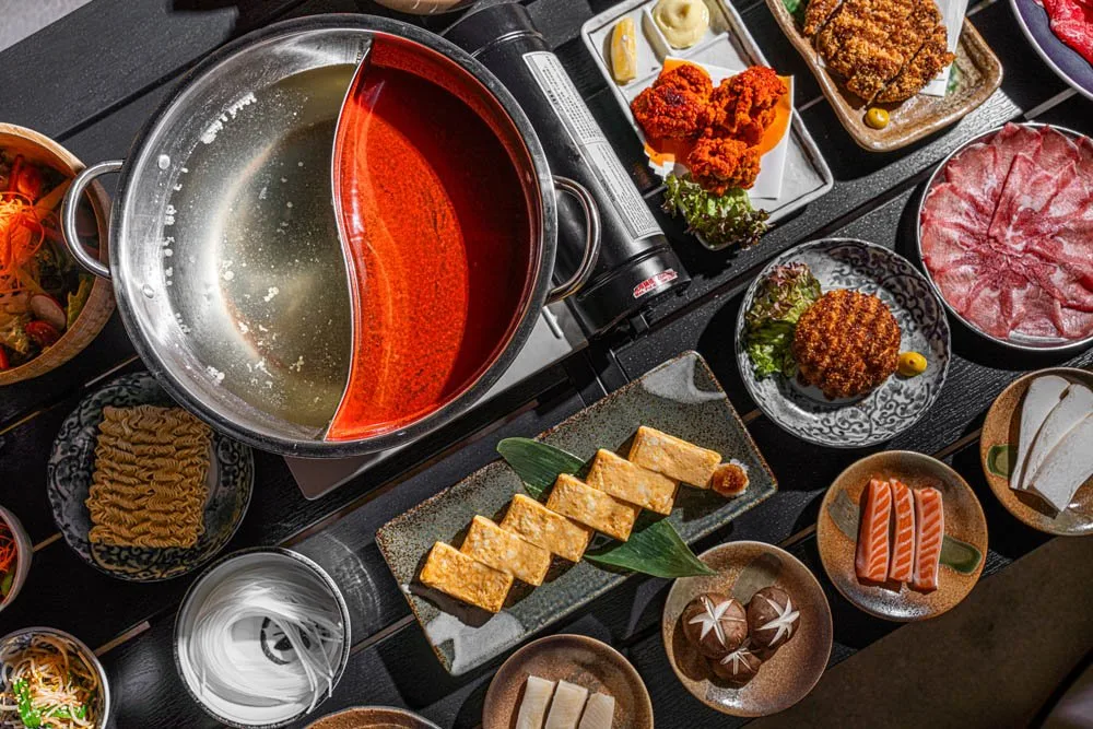 Overhead twin-broth hot pot surrounded by sashimi, noodles and sides