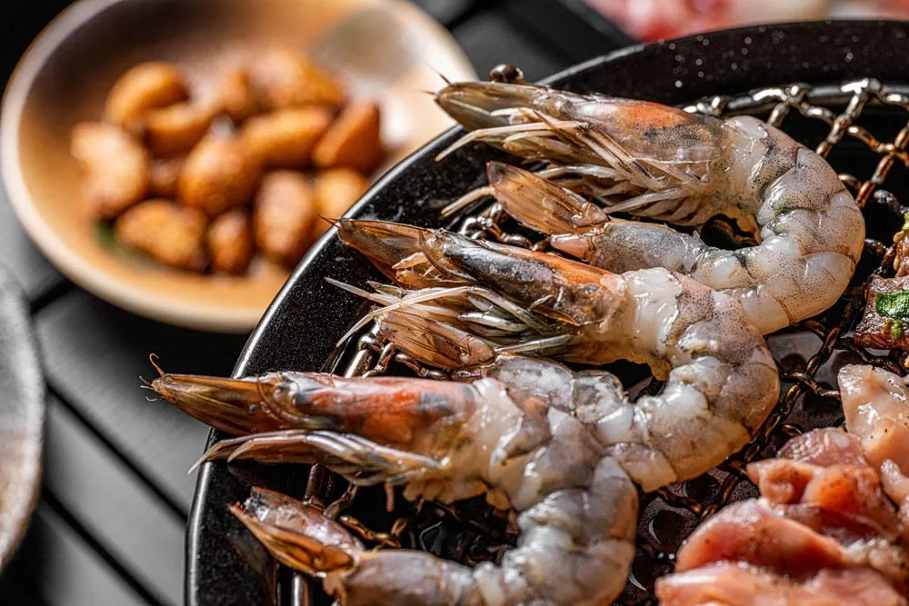 Fresh tiger prawns and skewers resting on a charcoal grill plate