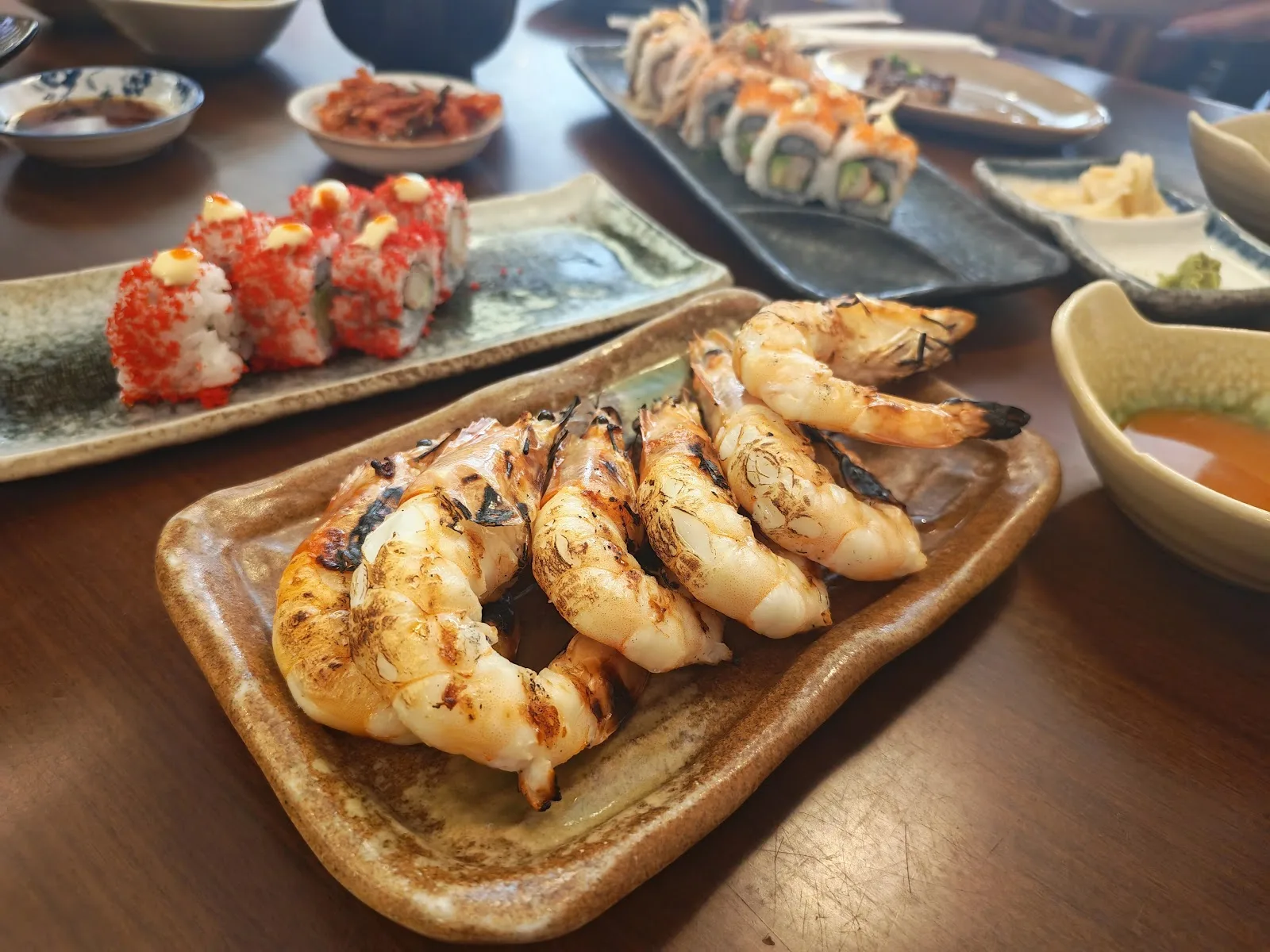 Plate of charcoal-grilled prawns beside maki rolls