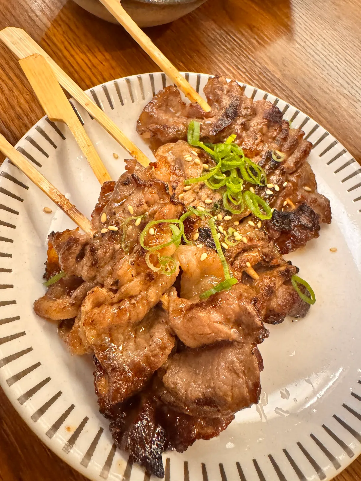 Plate of grilled pork skewers topped with spring onion and sesame