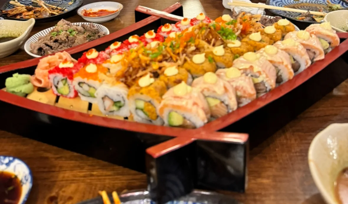 Wooden sushi boat loaded with colourful maki rolls topped with roe and spring onion
