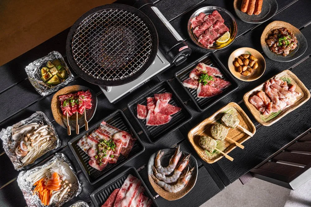 Overhead view of a yakiniku spread with raw marbled meats, prawns and mushrooms