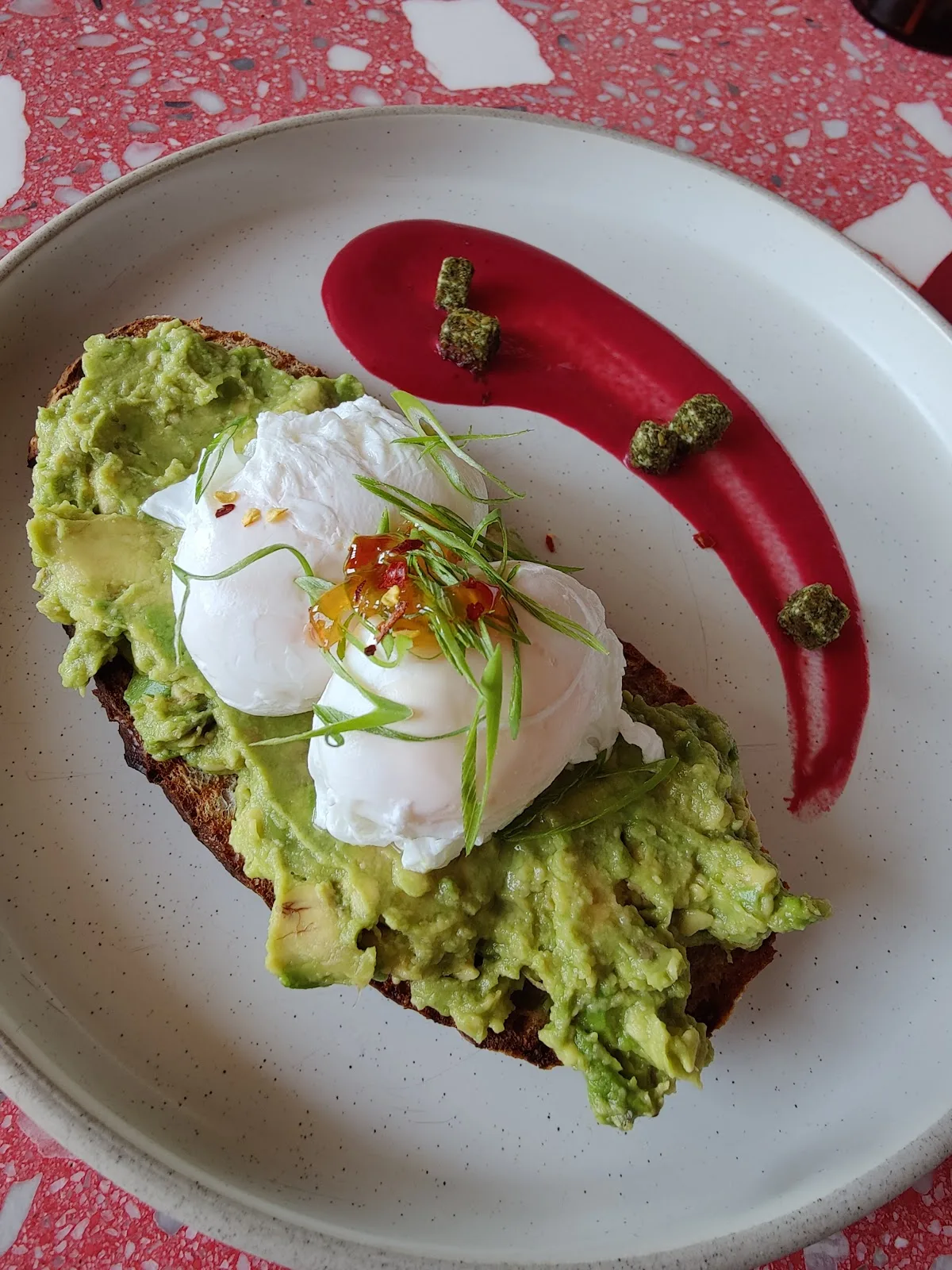 Avocado toast topped with poached eggs and chilli on a speckled plate