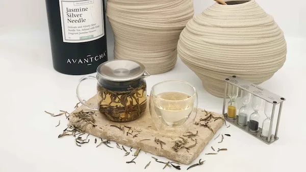 Loose-leaf jasmine tea steeping in a glass pot beside a paired cup