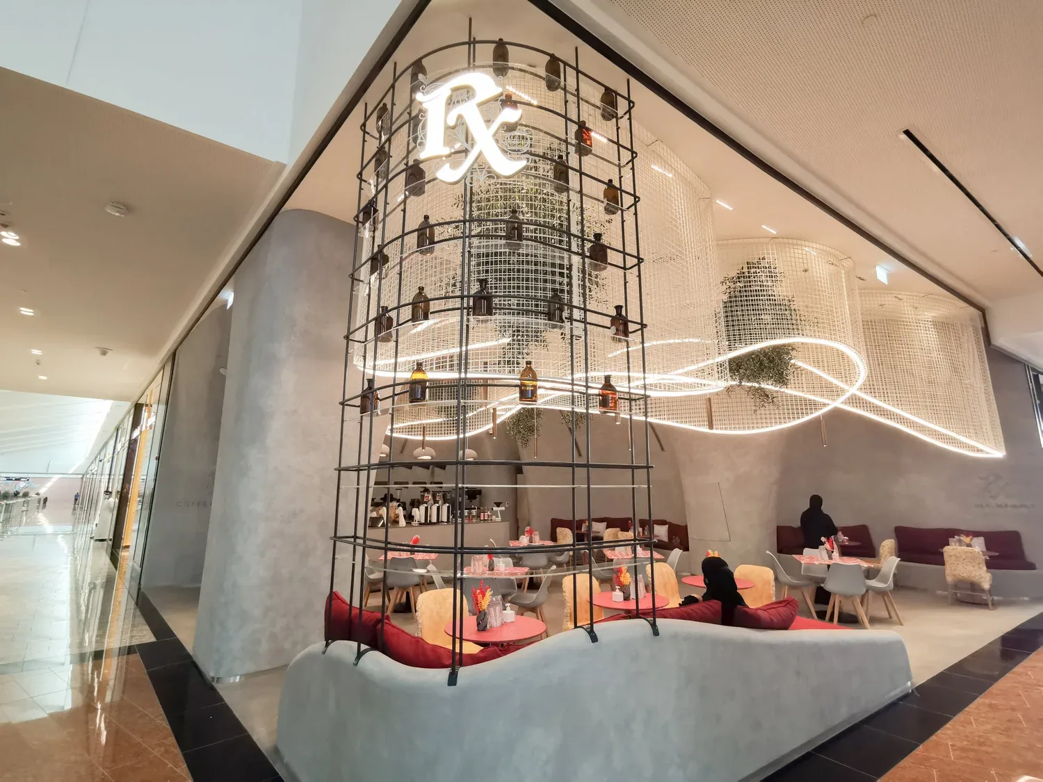A towering iron cage of apothecary bottles lit by a neon ℞ sign