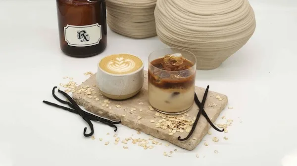 Hot latte and an iced coffee served on a stone board beside an Rx apothecary jar