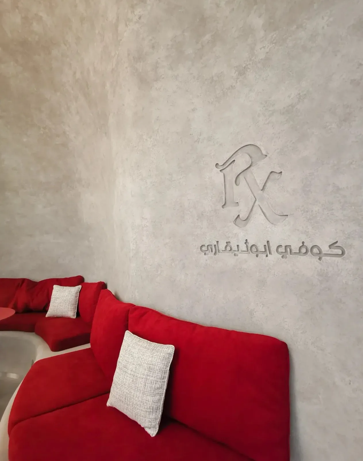 The embossed ℞ monogram on a polished concrete wall above red velvet seating