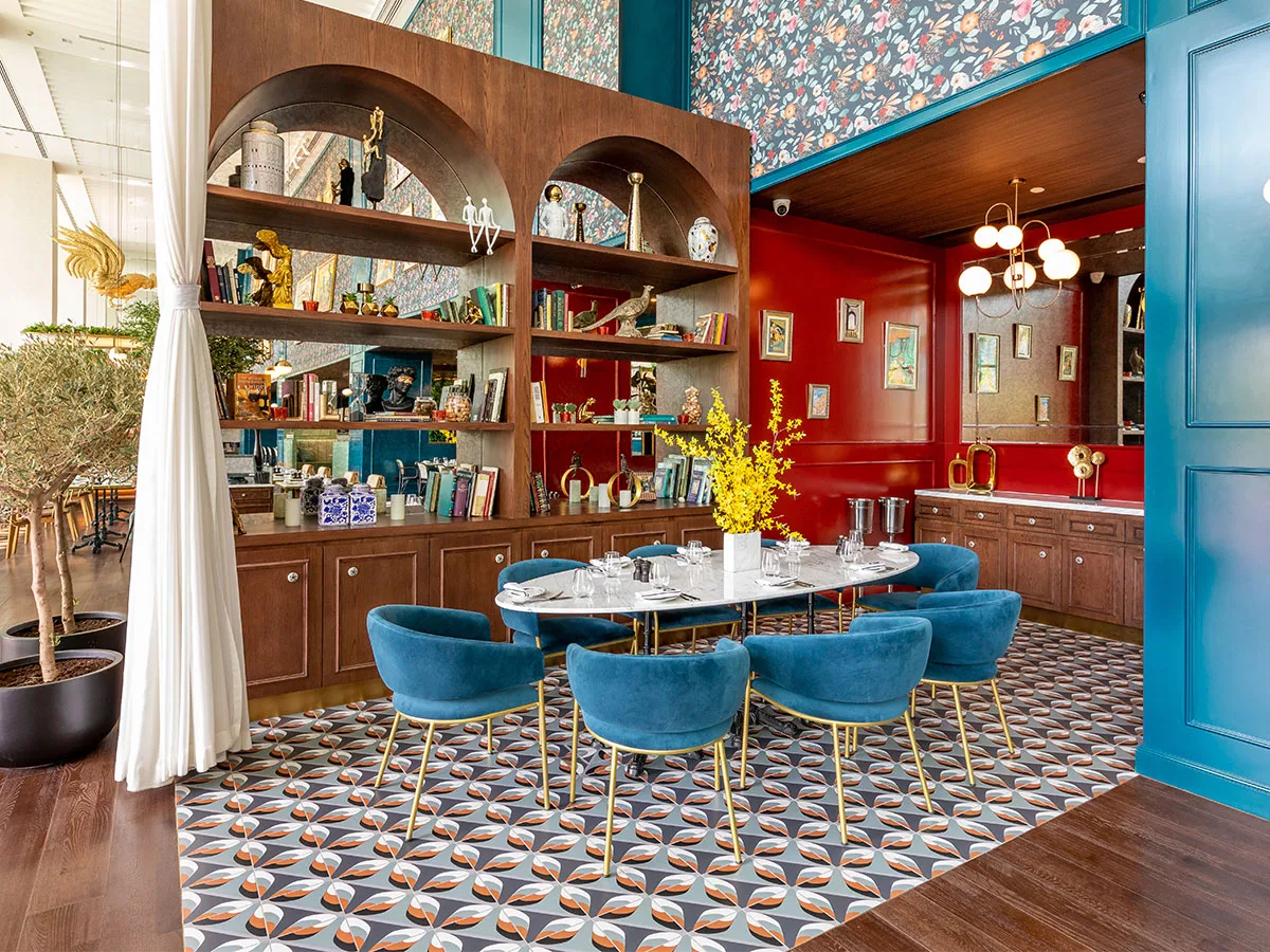 Couqley interior with teal velvet chairs, a red feature wall and an arched, bottle-lined bar