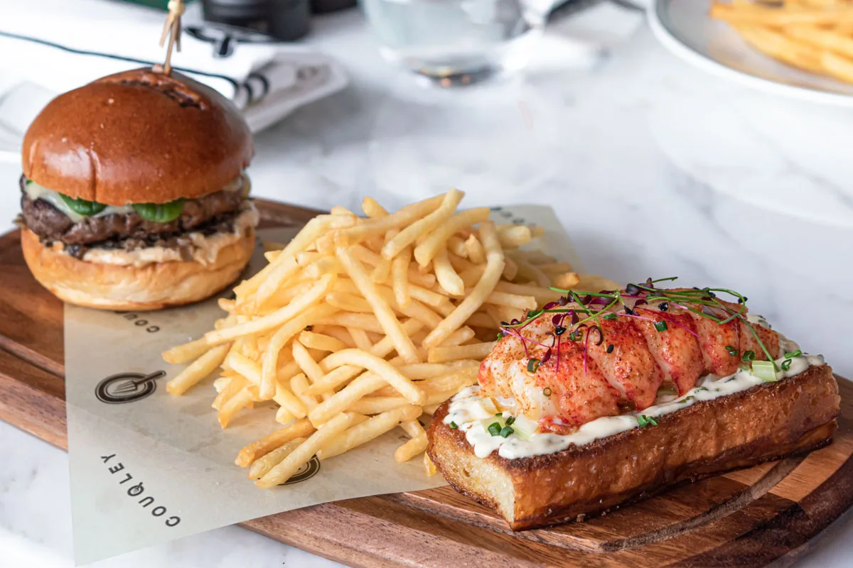 Beef burger with fries and a lobster roll on a marble board
