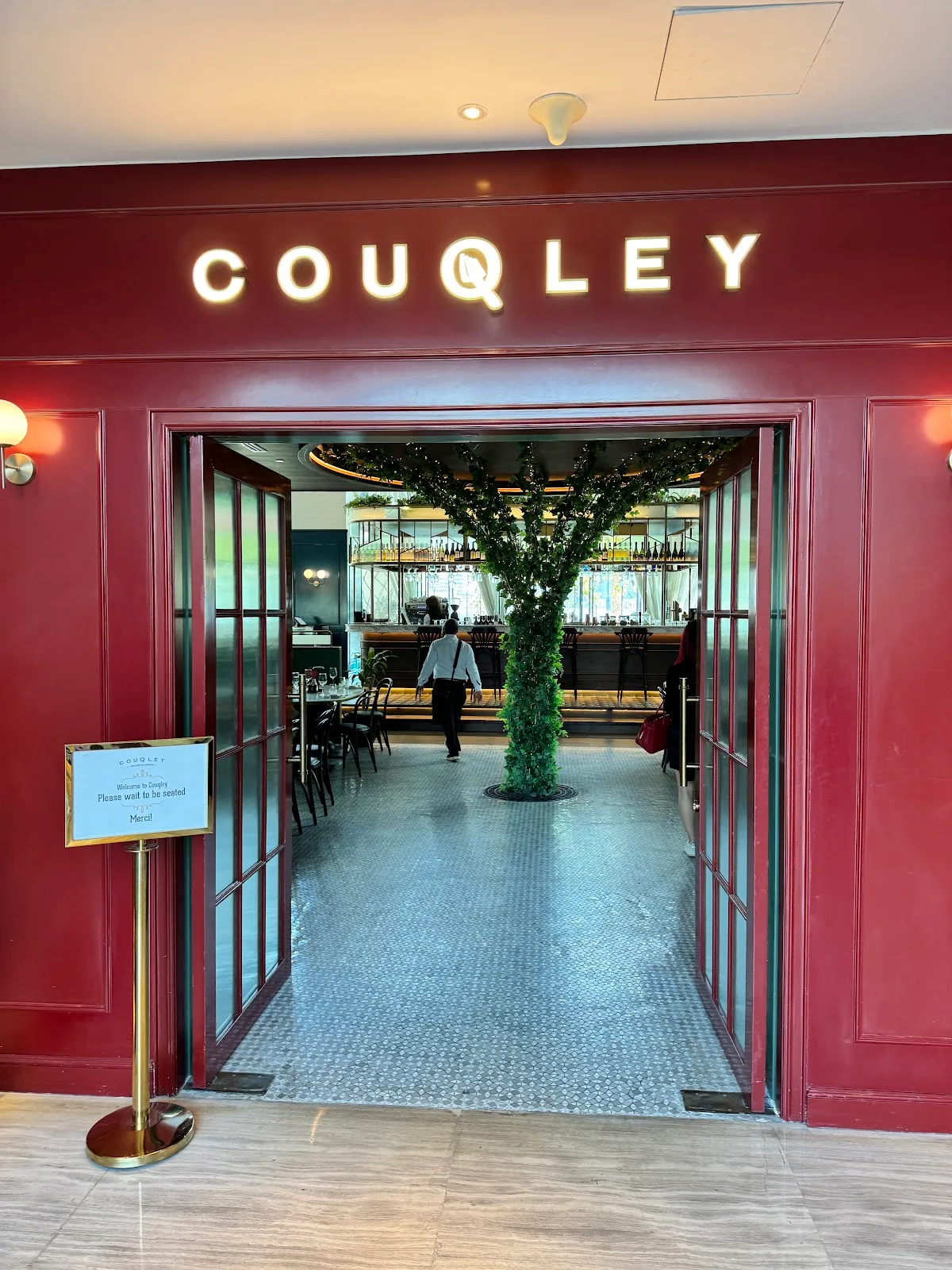 Couqley's red entrance facade with a doorway framing a courtyard tree