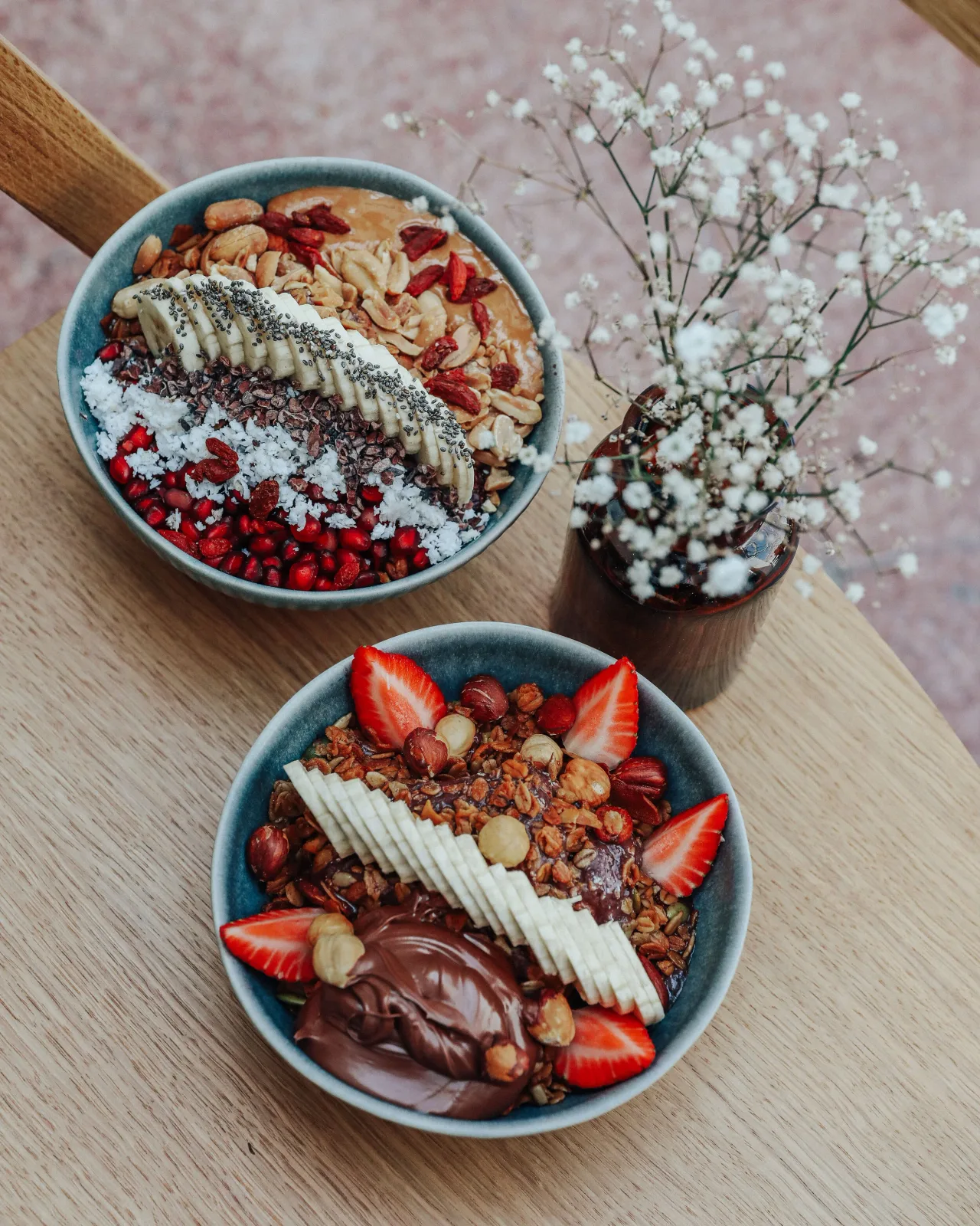 Two açaí bowls topped with banana, granola, berries and seeds