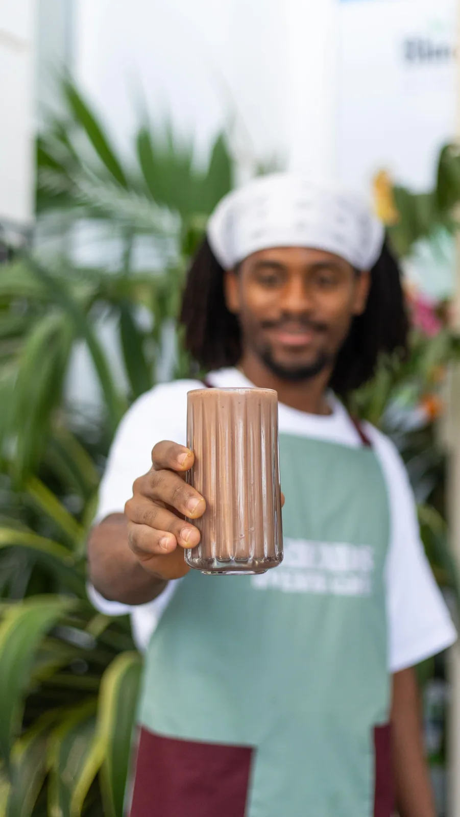 Barista holding out a fresh smoothie among tropical plants