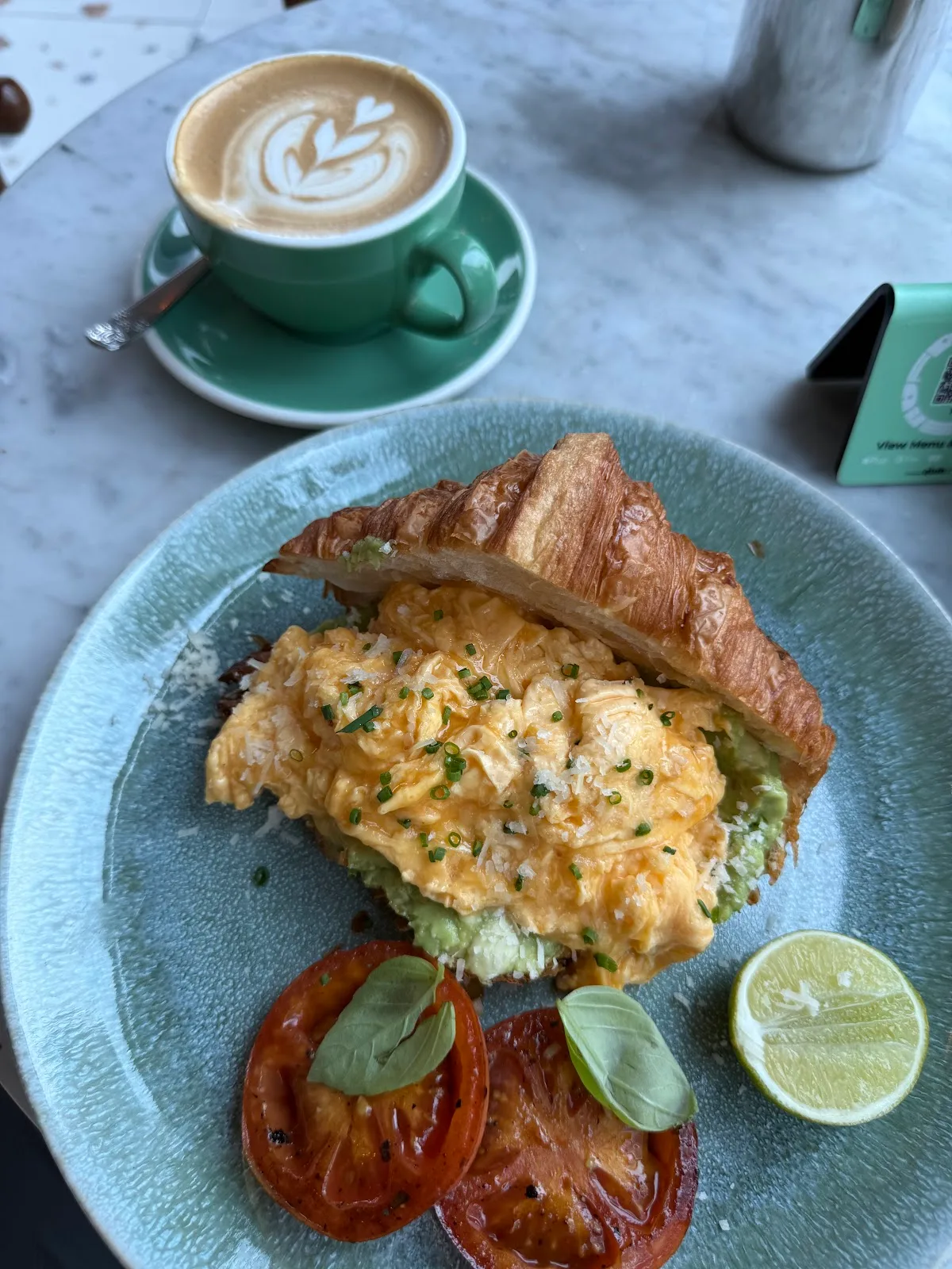 Scrambled egg croissant with grilled tomato and a flat white