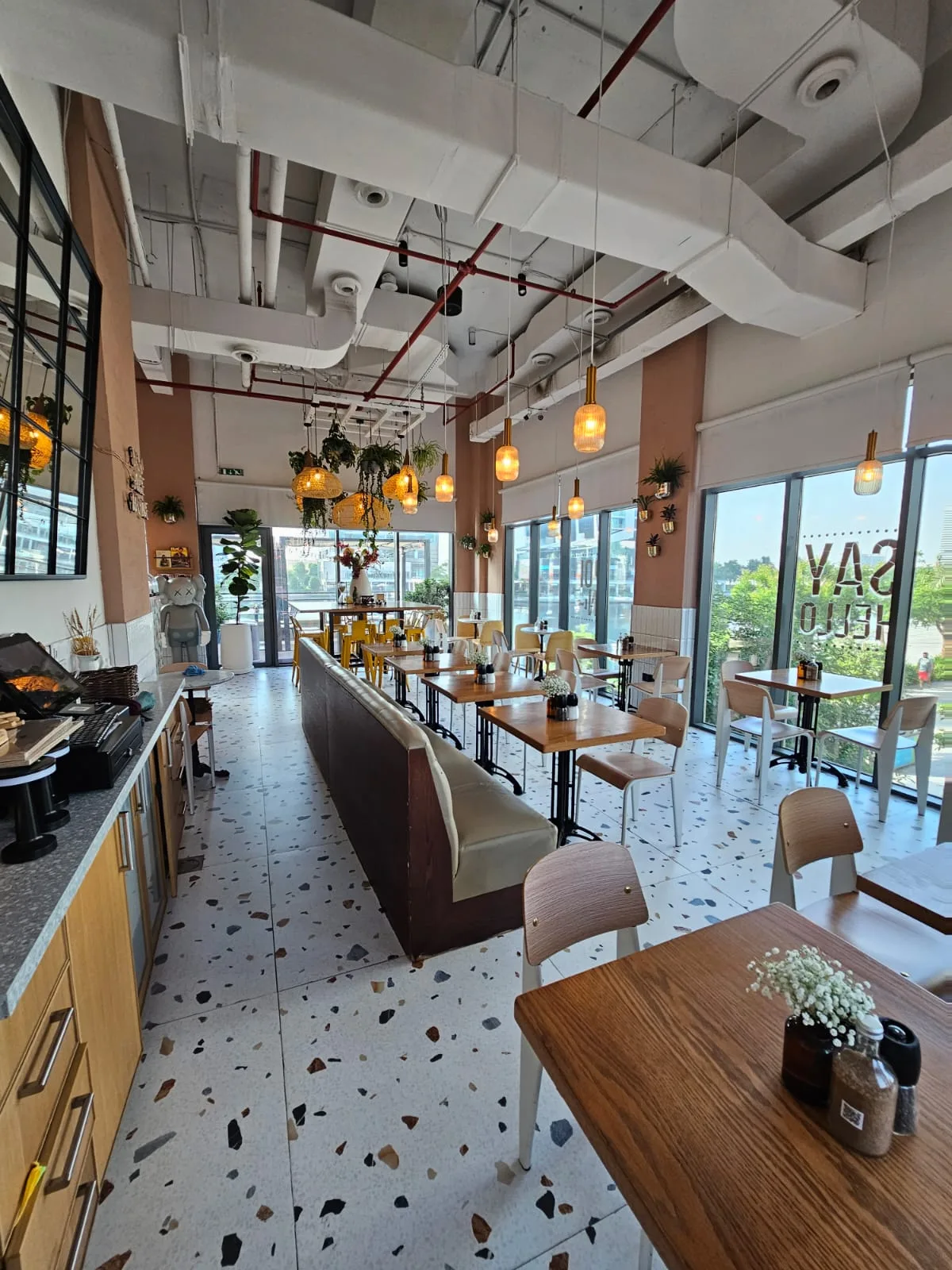 Wide view of the cafe with terrazzo floor, yellow chairs and Say Hello window decal