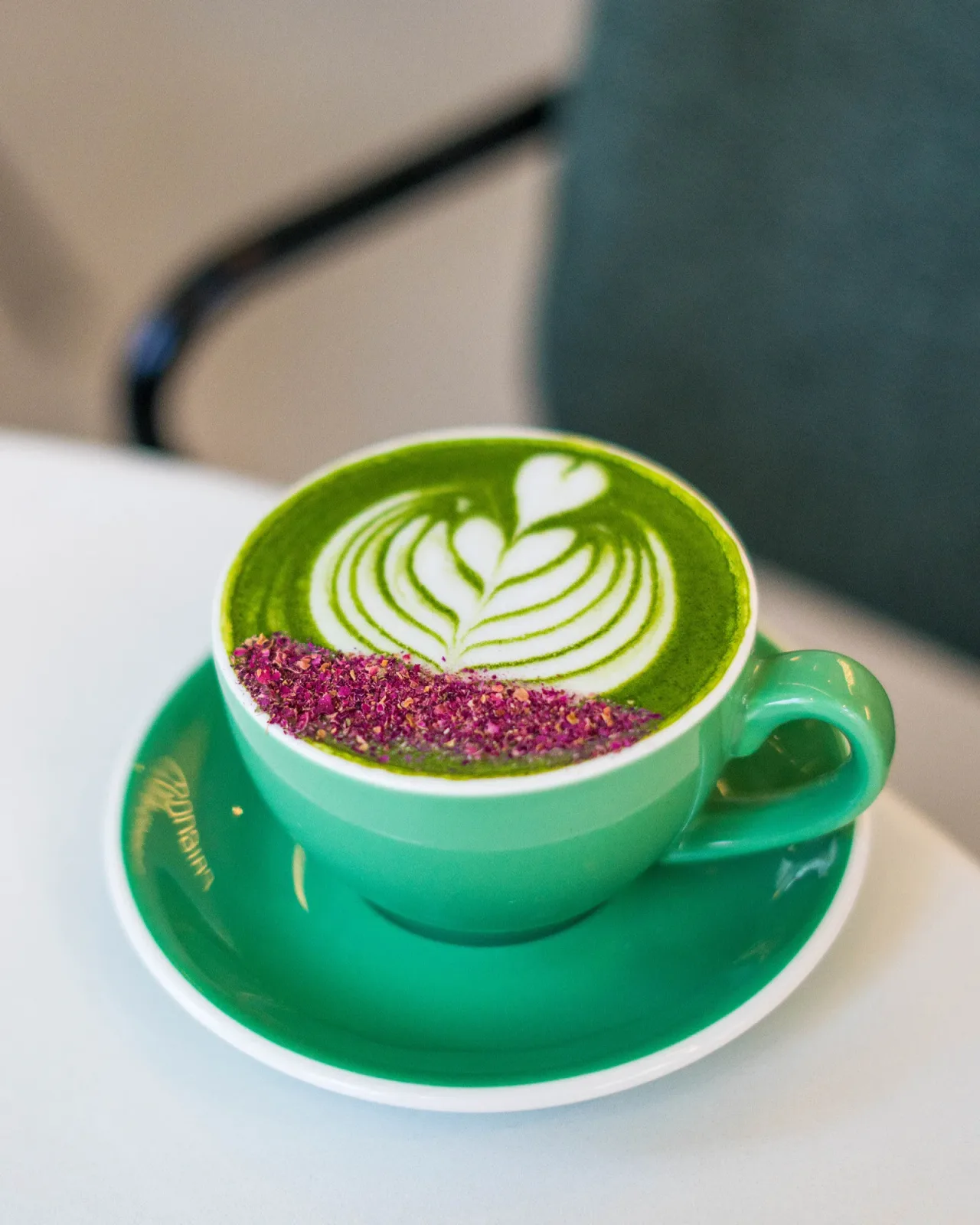 Green matcha latte with leaf art and rose petals in a green cup